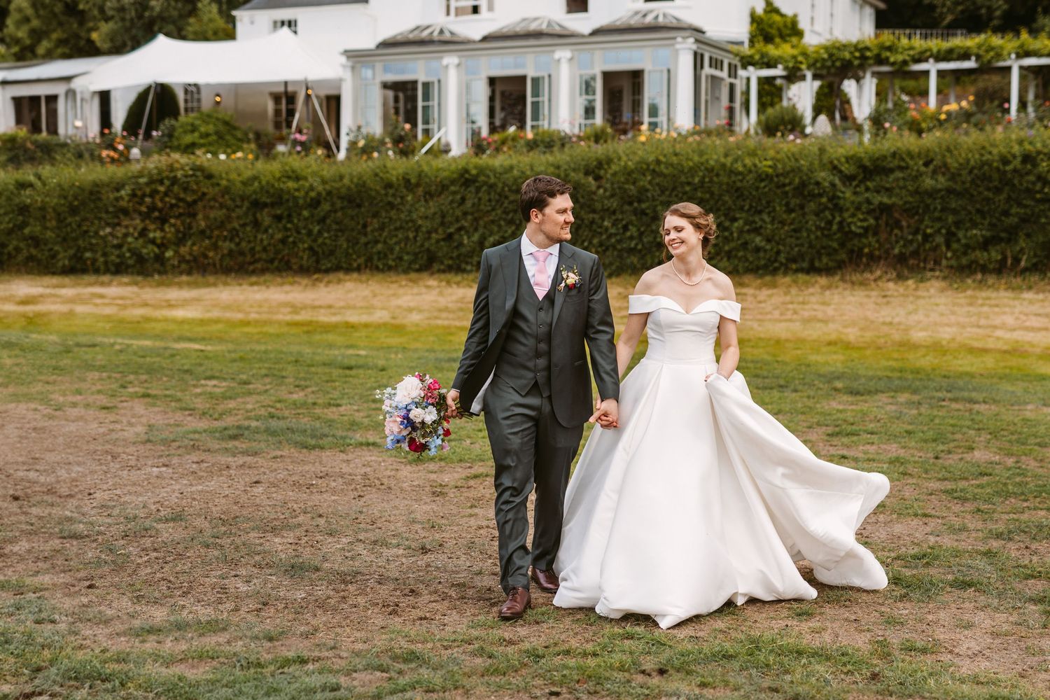 Beautiful bride and Groom laughing together walking across lawn at Remenham Court Henley on Thames towards the river