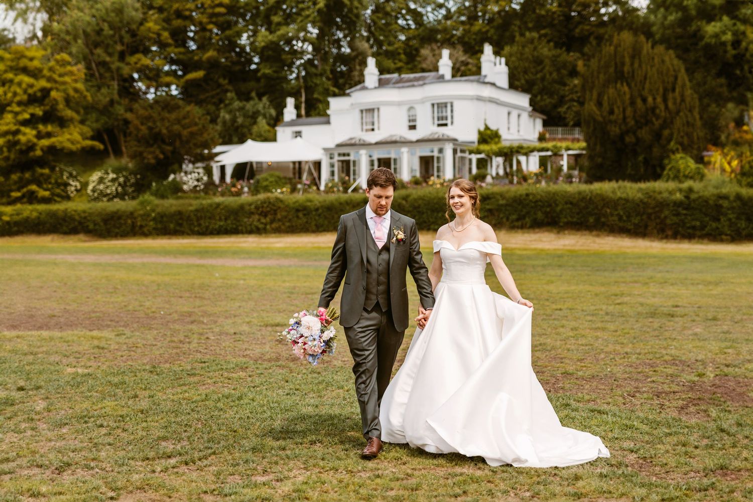 Beautiful bride and Groom laughing together walking across lawn at Remenham Court Henley on Thames towards the river