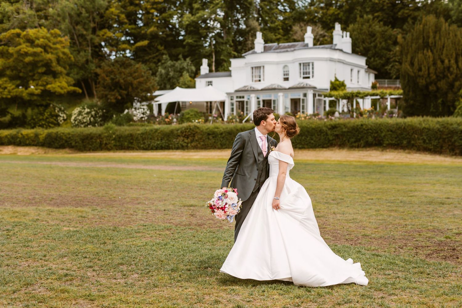 Beautiful bride and Groom laughing together walking across lawn at Remenham Court Henley on Thames towards the river