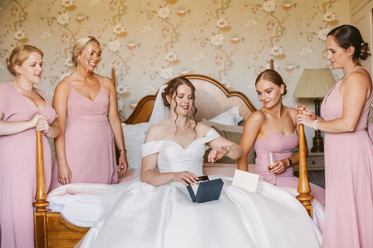 Bride surrounded by bridesmaids as she opens a gift watch from husband to be