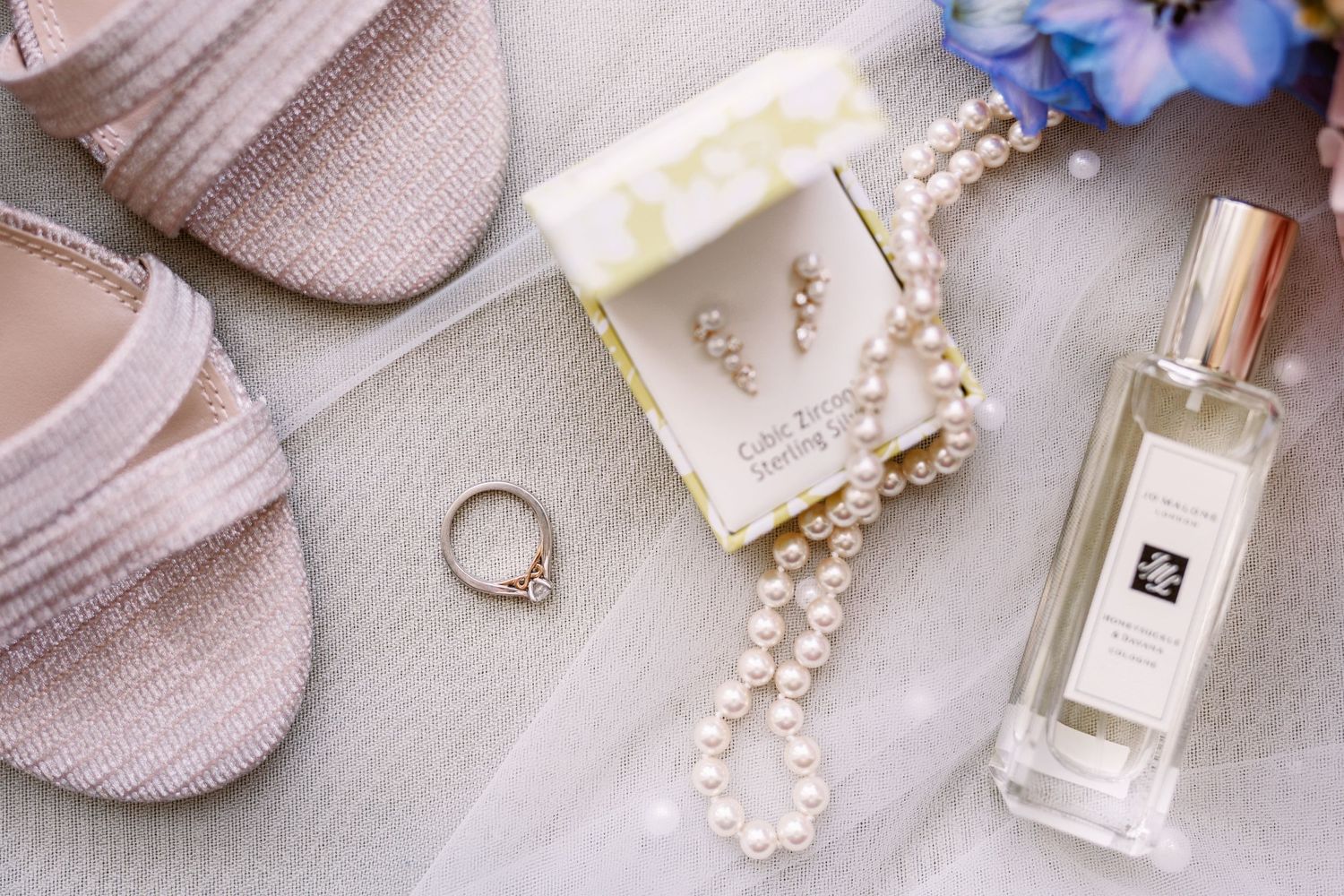 Brides details in flat lay showing engagement ring perfume jewellery shoes bouquet pretty pinks and blues