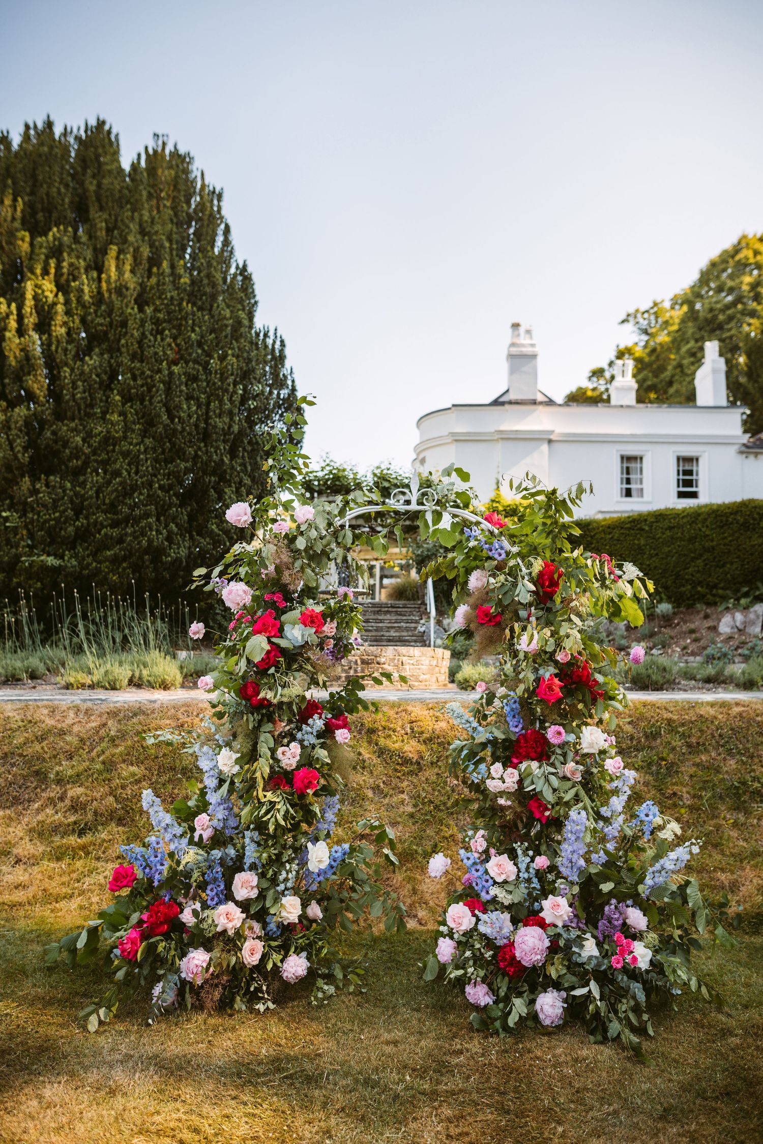 Stunning joyful flower arch bursting with vibrant colours with Remenham Court wedding venue behind