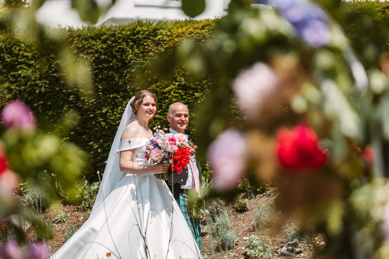 Bride arriving with Father dad walks beautiful daughter up the aisle surrounded by bold colourful flowers summers day