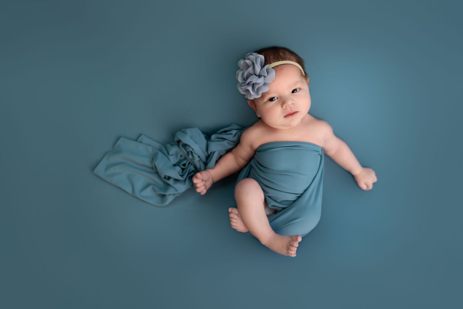 Newborn baby wearing soft blue wrap during professional photography session.