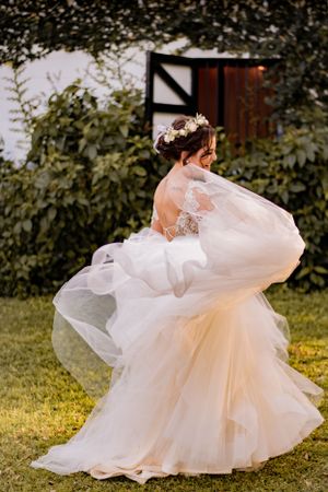 Bride in flowing tulle wedding gown twirling outdoors with lush greenery backdrop.