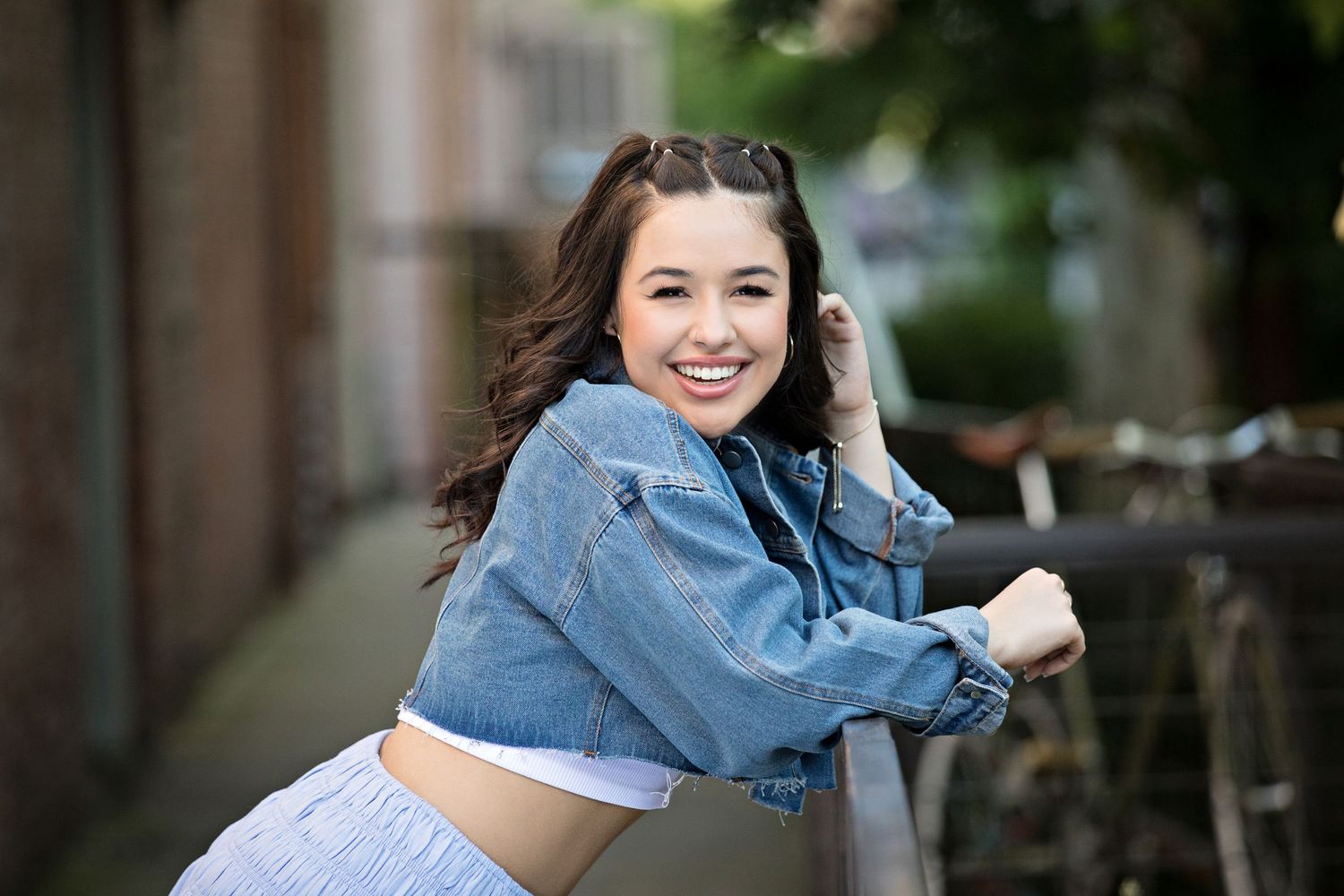 Casual portrait of woman in denim jacket posing playfully outdoors.