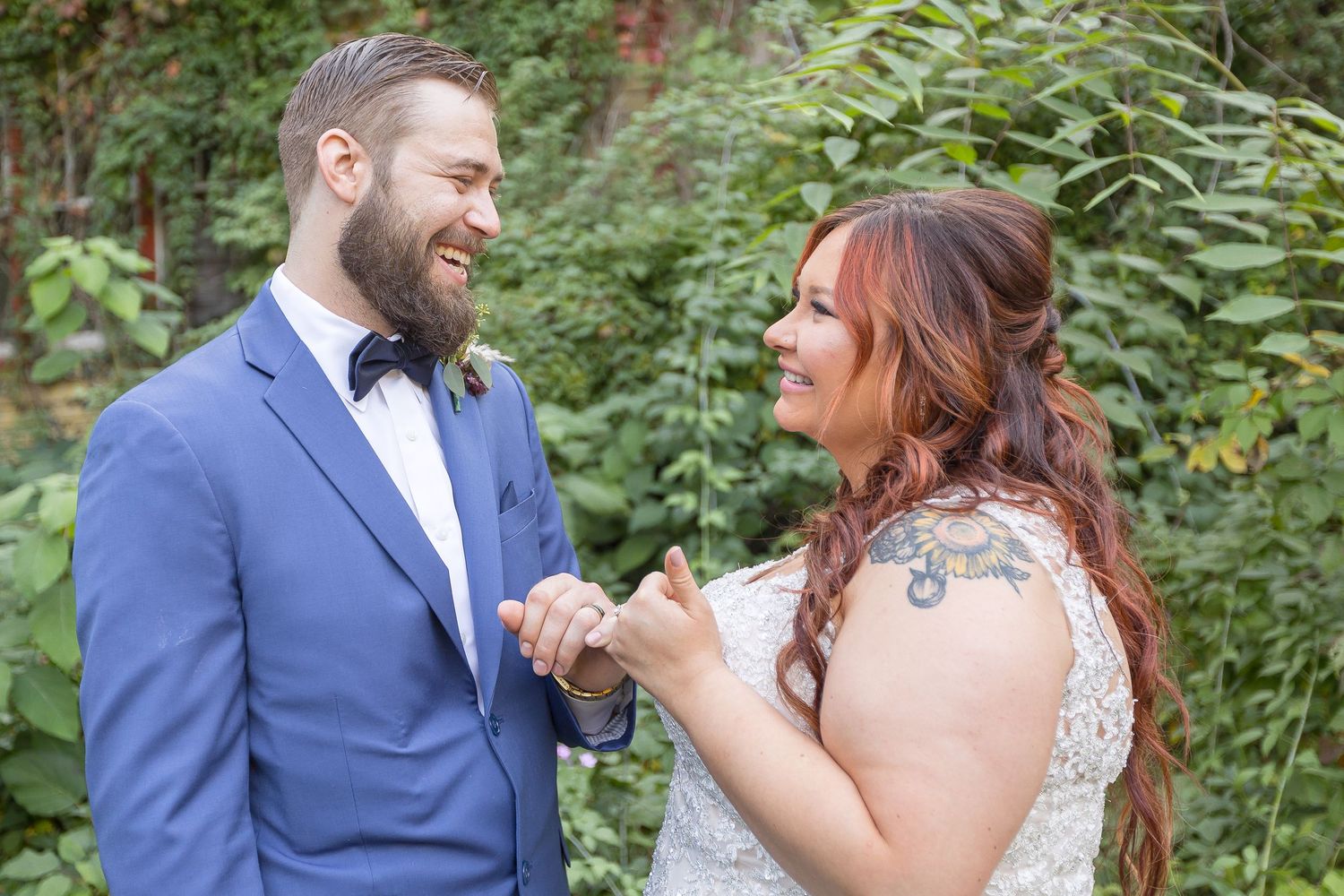 Two people in wedding attire laugh together during outdoor portrait session in a garden setting.