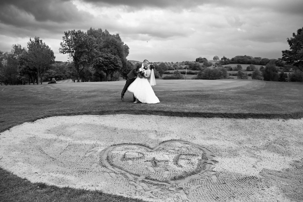 Black and white wedding photo with dramatic clouds and heart drawn in sand.