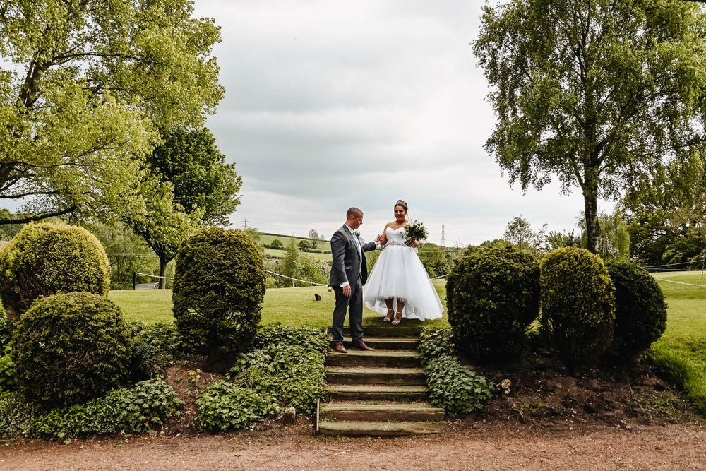 Garden wedding photo with couple posing on stone steps surrounded by greenery.