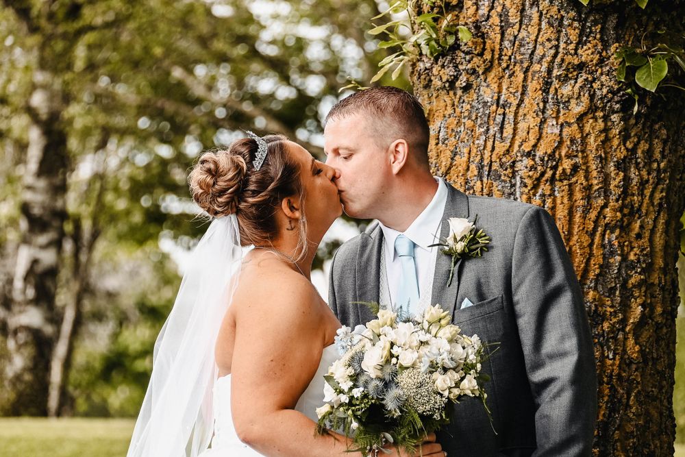Romantic wedding couple embracing against a rustic tree trunk backdrop.