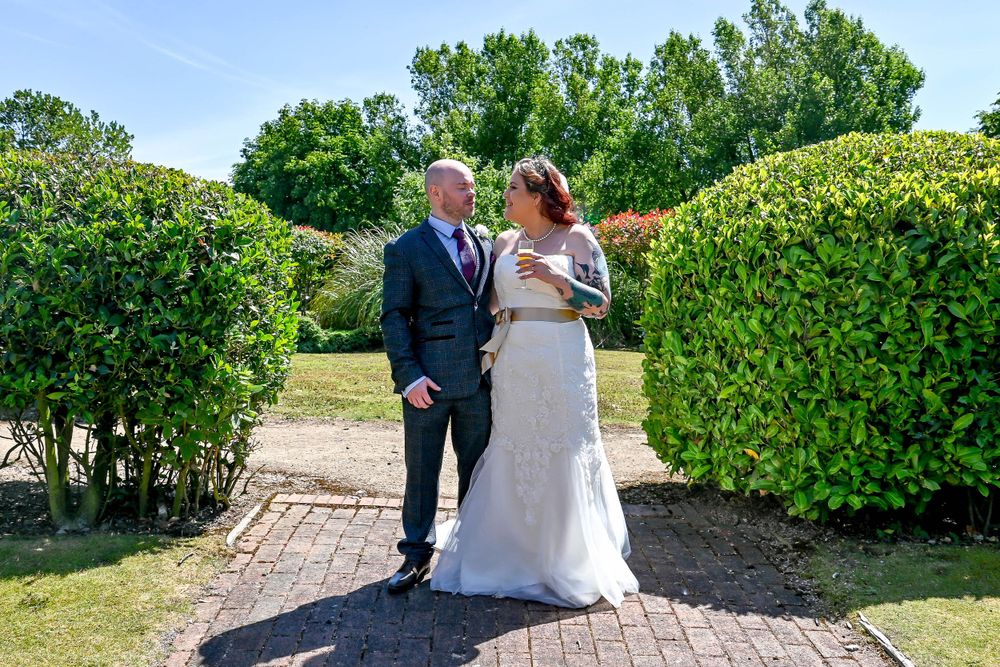 Wedding couple walking along landscaped garden path with manicured hedges.