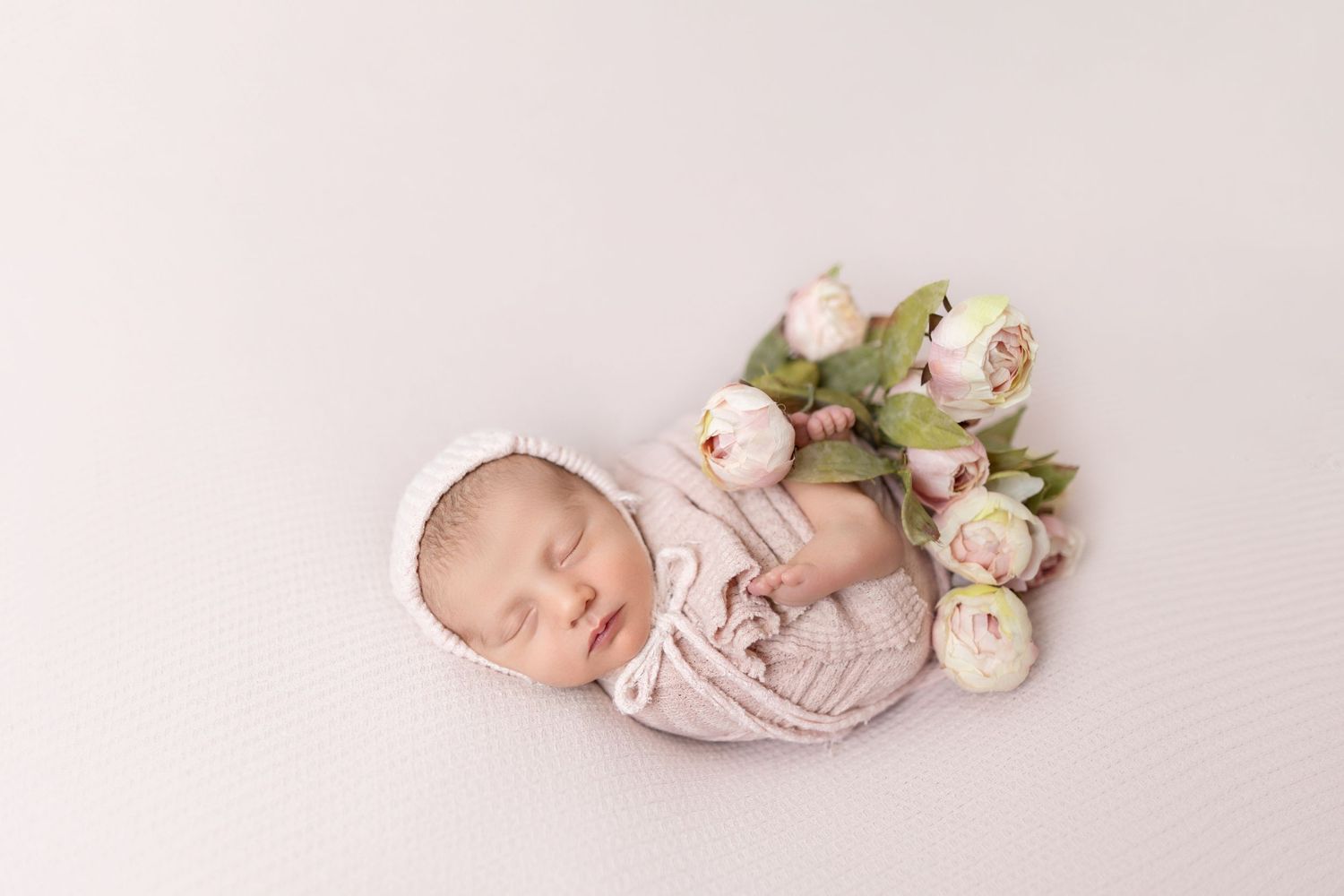 Newborn photography with baby wrapped in pink beside delicate roses.