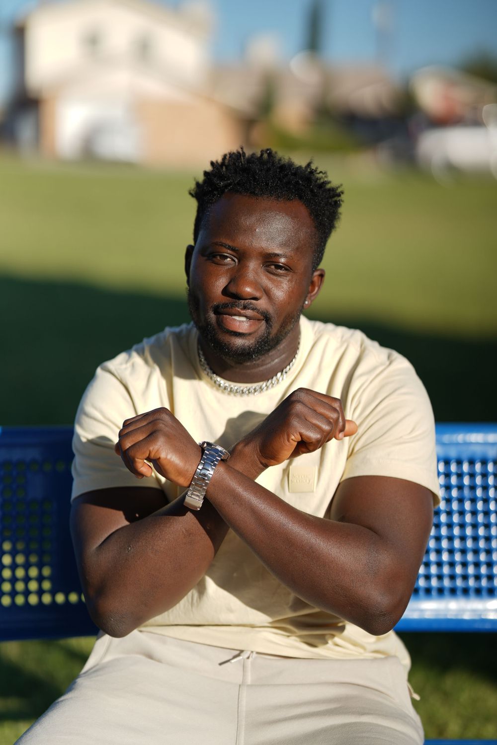 Portrait of person in cream colored outfit sitting on blue bench outdoors.