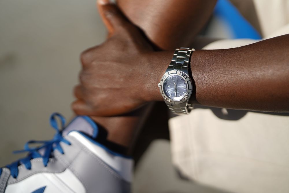 Detailed shot of silver wristwatch against arm with blue and white sneaker in background.