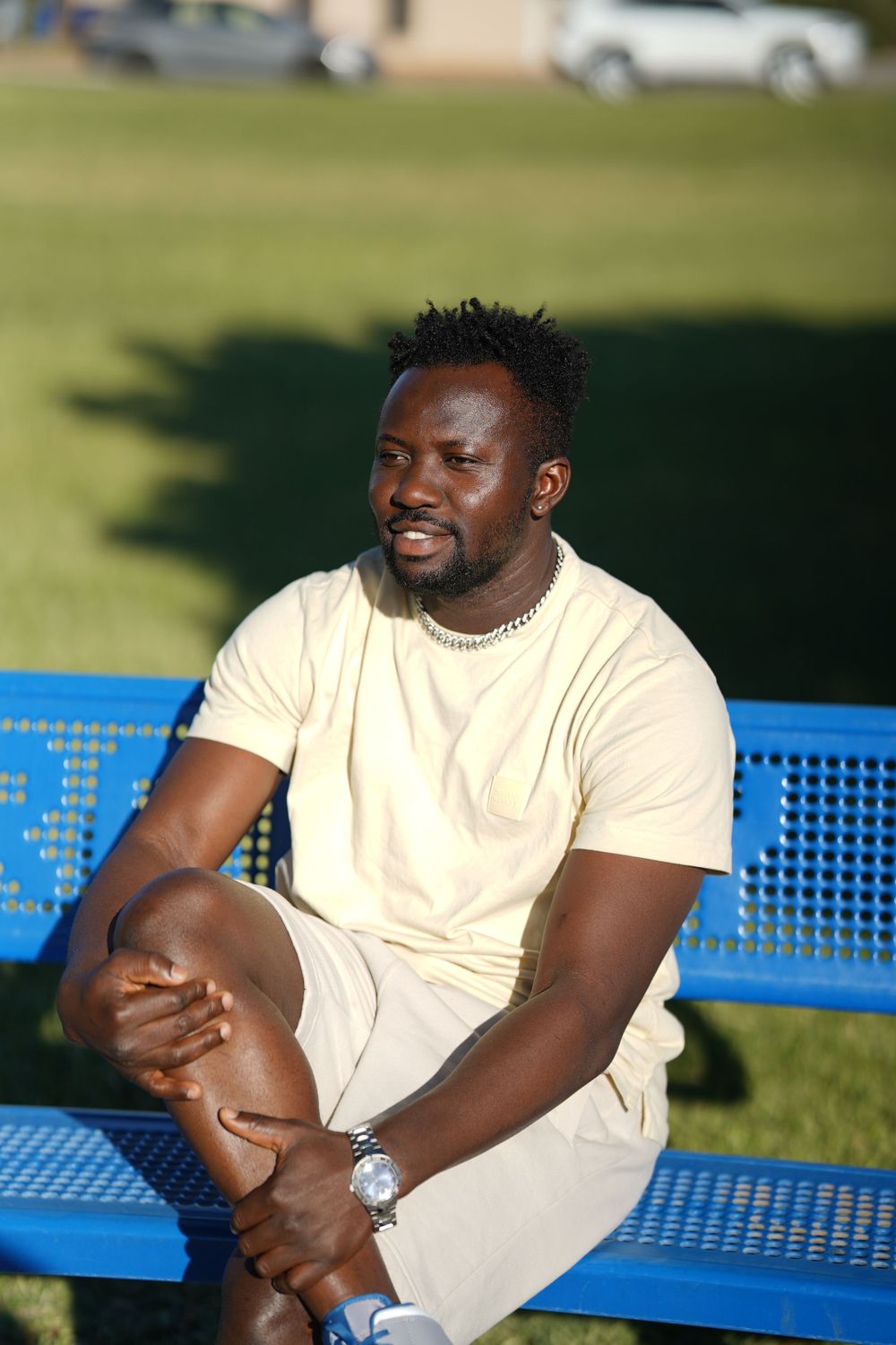 Person relaxing on a blue bench outdoors wearing cream colored outfit with a silver watch.