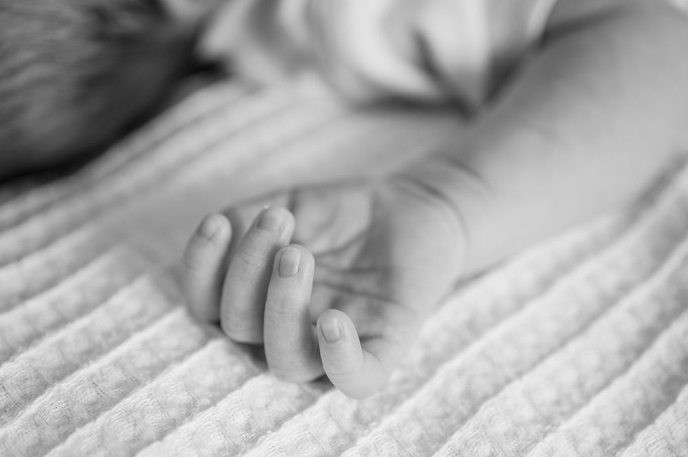 Close-up black and white photograph showing a tiny newborn baby's hand resting on soft textured fabric.