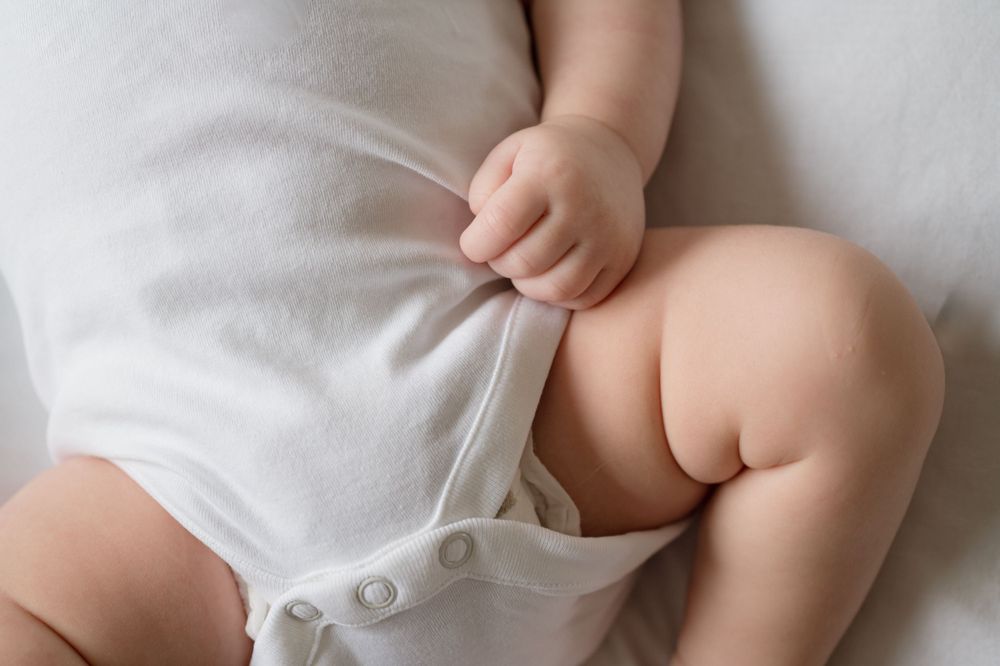 Close-up of baby wearing white onesie with delicate buttons and soft fabric details.