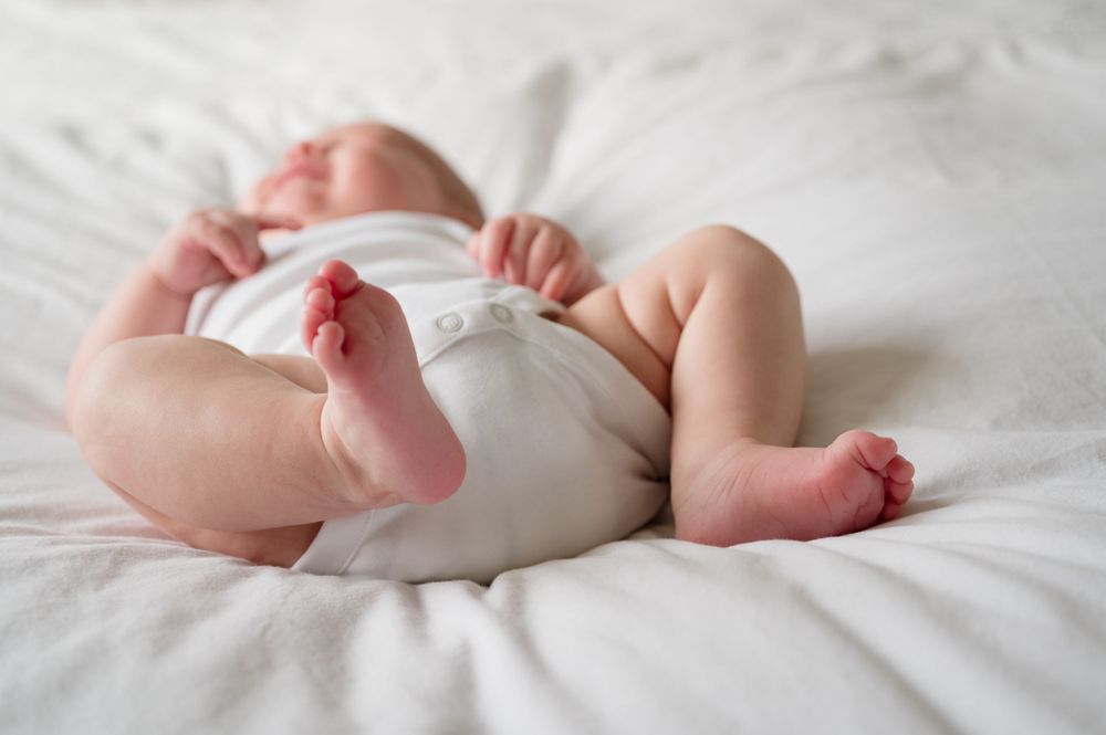 Tiny baby feet peeking out from white blankets on a soft bed.