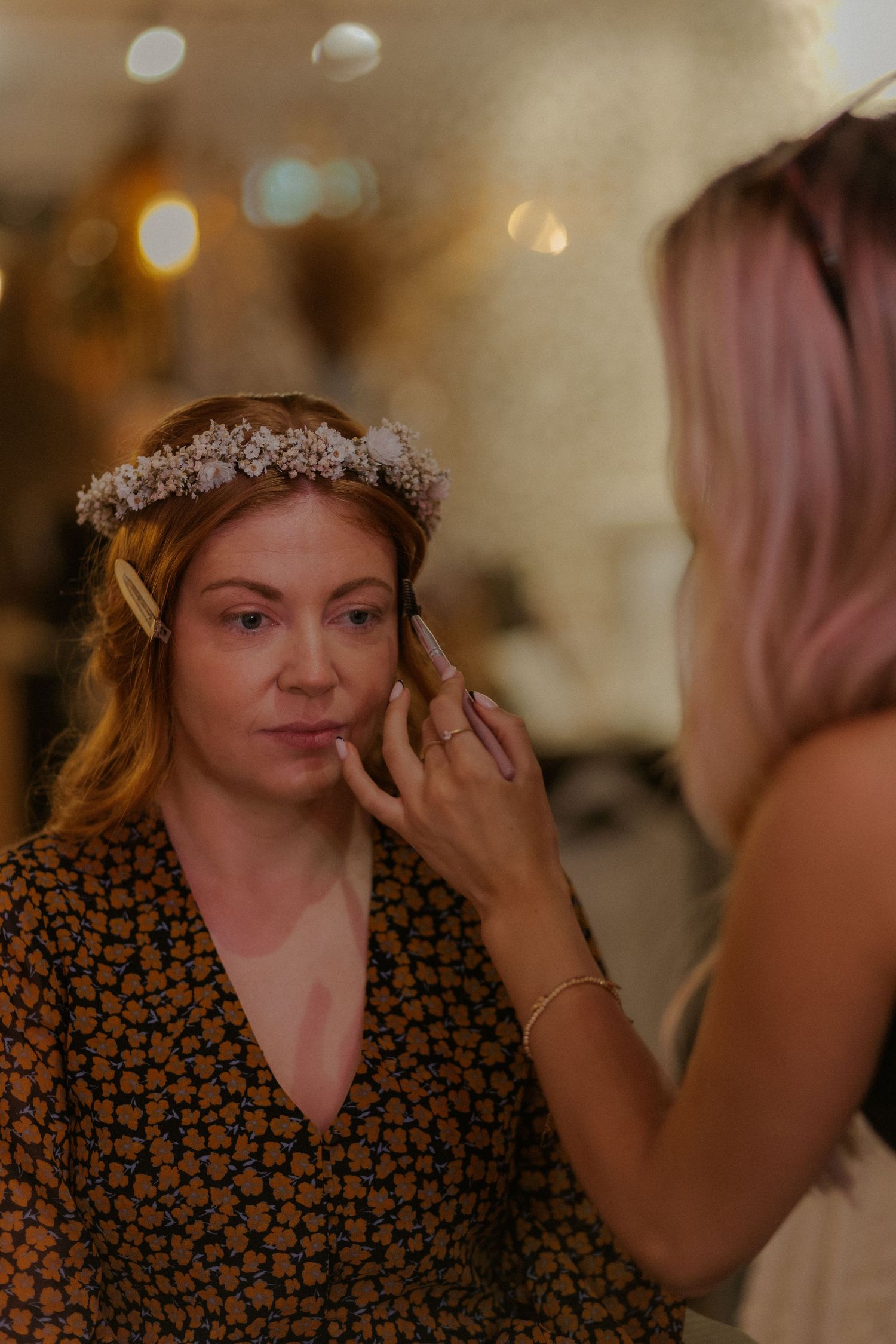 Intimate beauty preparation moment with crystal crown and floral print robe in warm lighting.