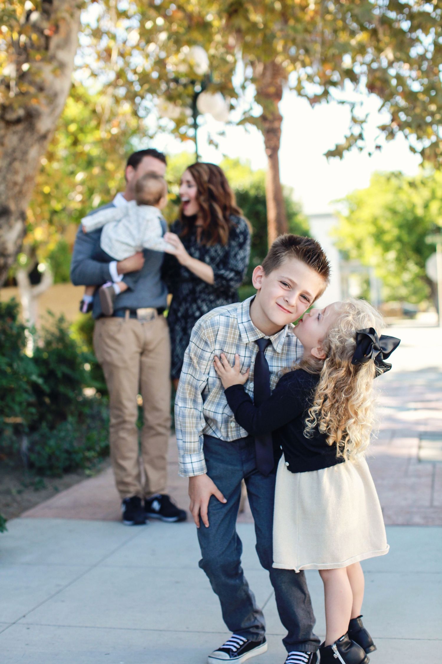 Family portrait on sidewalk with playful children in foreground and parents in background.