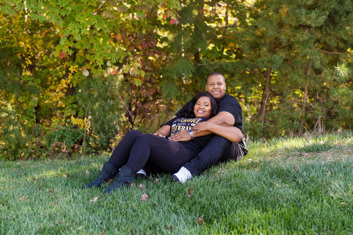 A couple relaxes together on a grassy hillside surrounded by autumn foliage.