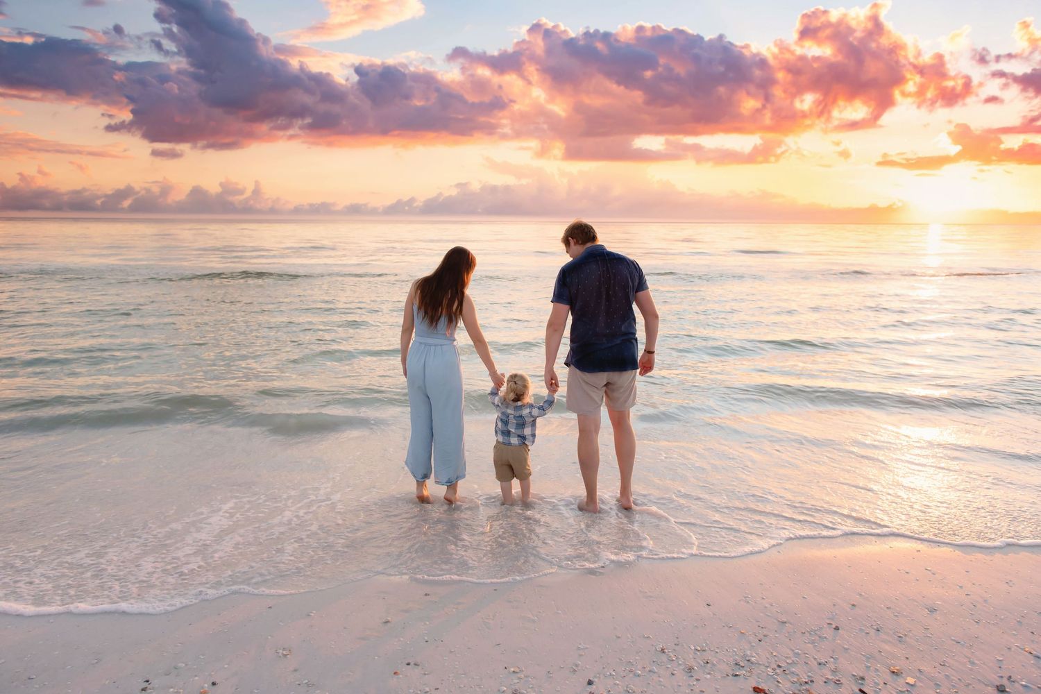 Family walking together along shoreline during golden hour sunset.