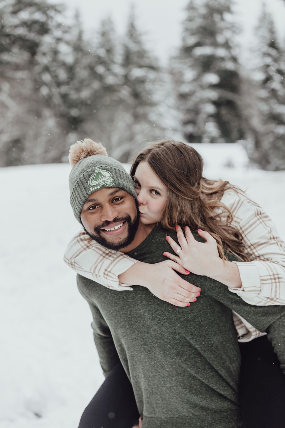 A couple plays piggy back in the snow during an engagement session with Pamela Clark