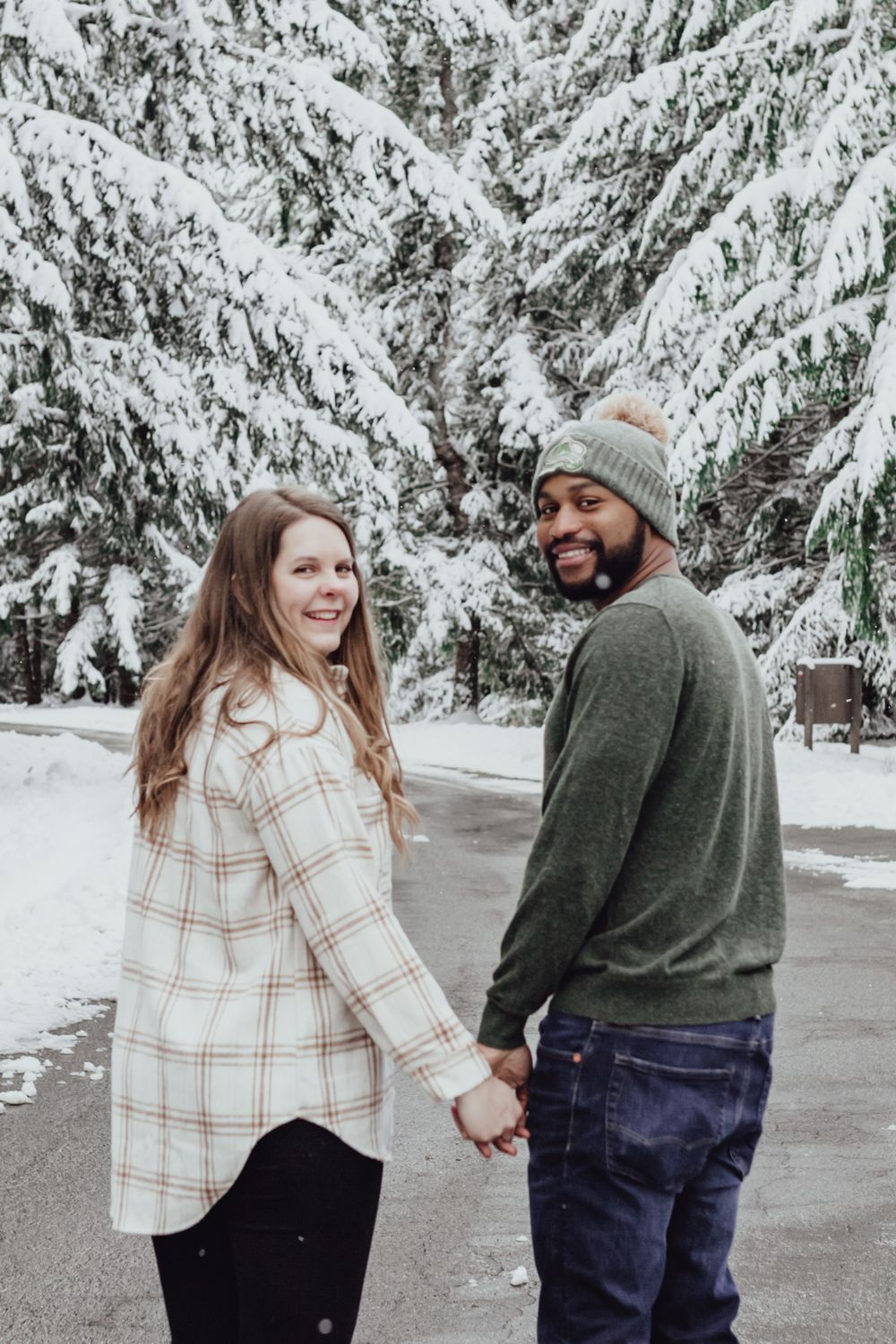 A couple walks while looking at the camera in the snow during an engagement session with Pamela Clark