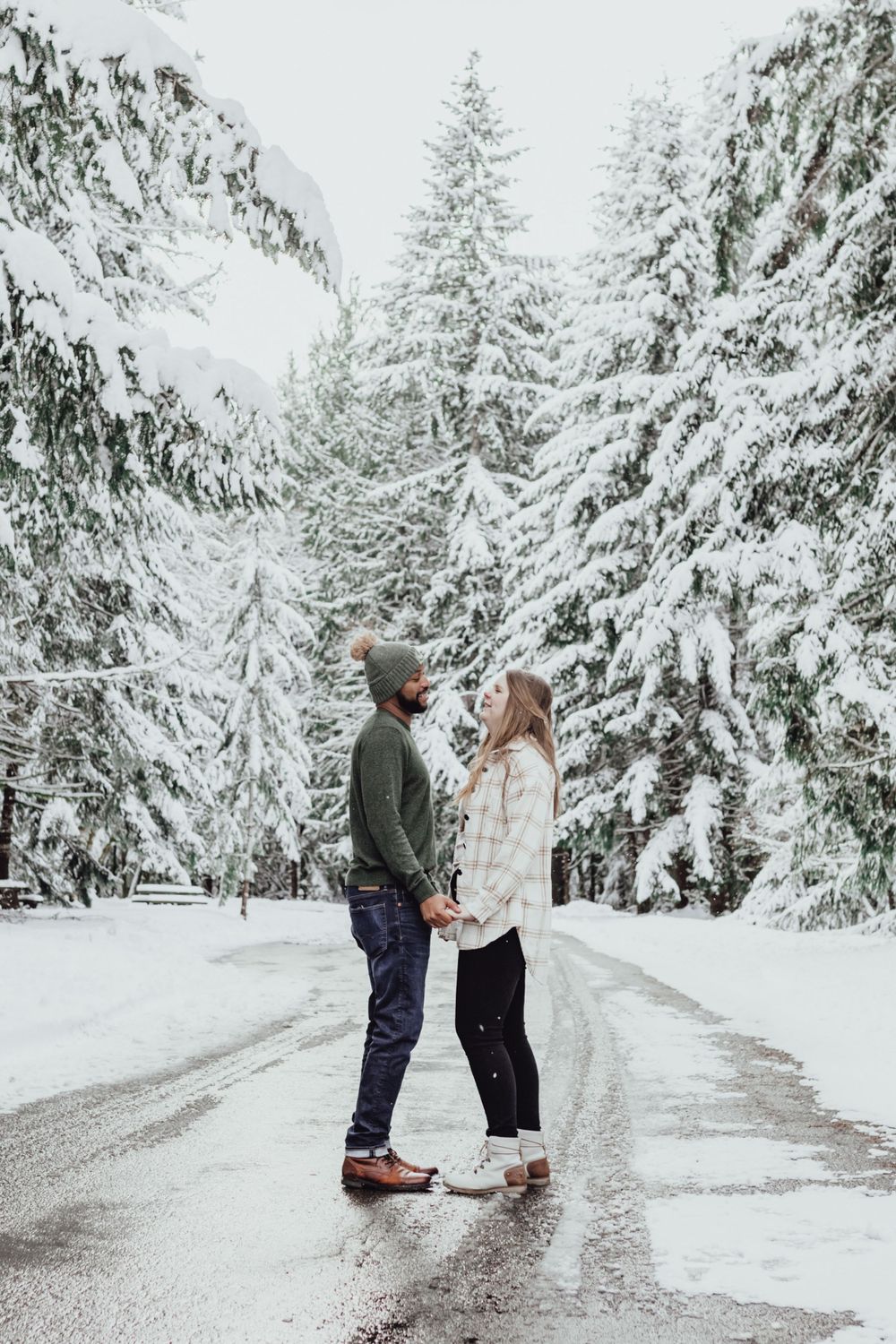 A couple holds hands while looking at each other in the snow during an engagement session with Pamela Clark