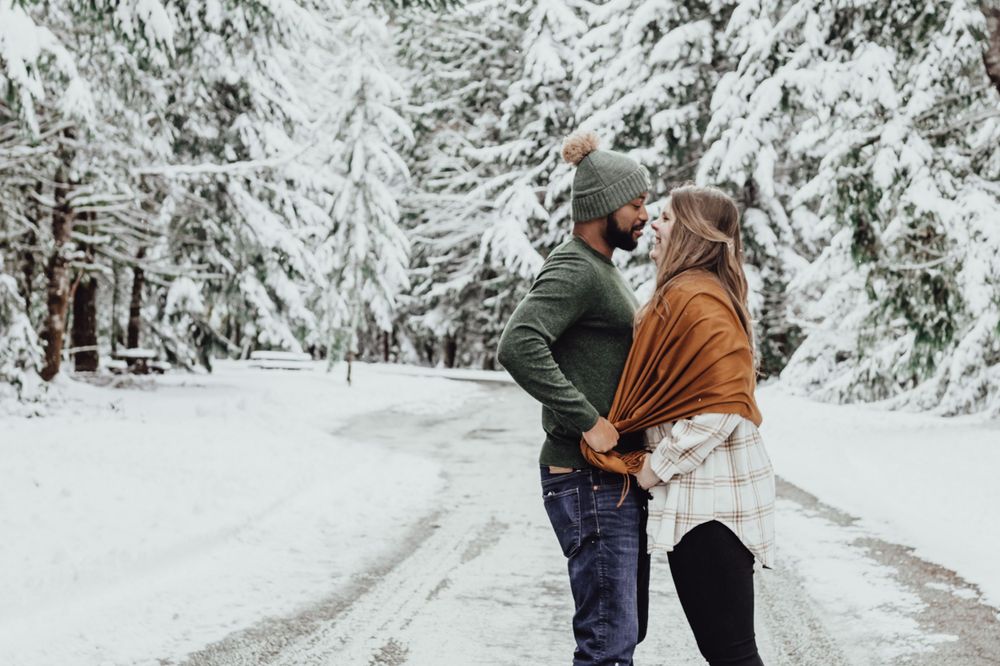 A couple holds hands and talks to each other in the snow during an engagement session with Pamela Clark