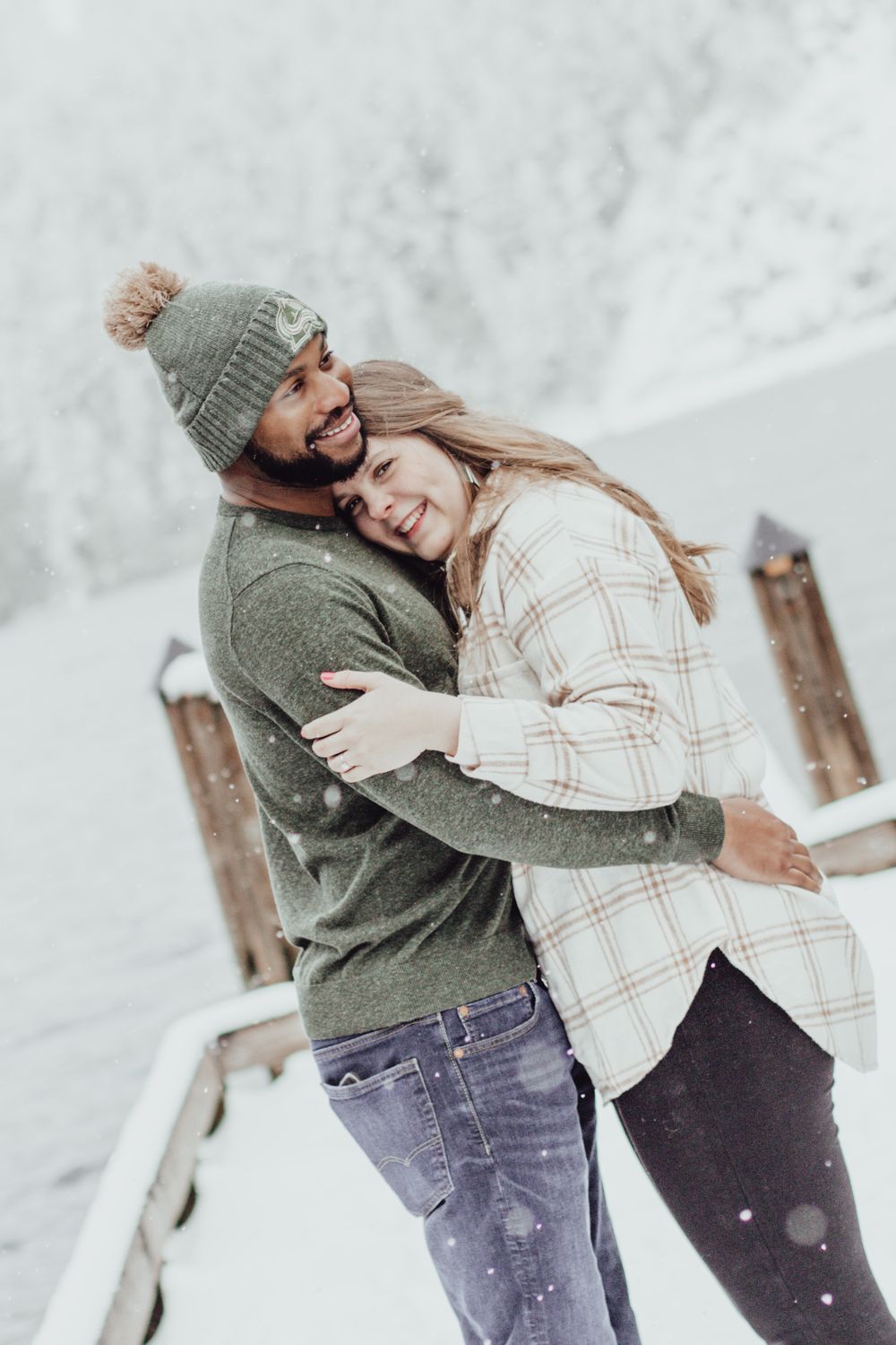 A couple hugs while looking at the camera on a snowy pier during an engagement session with Pamela Clark