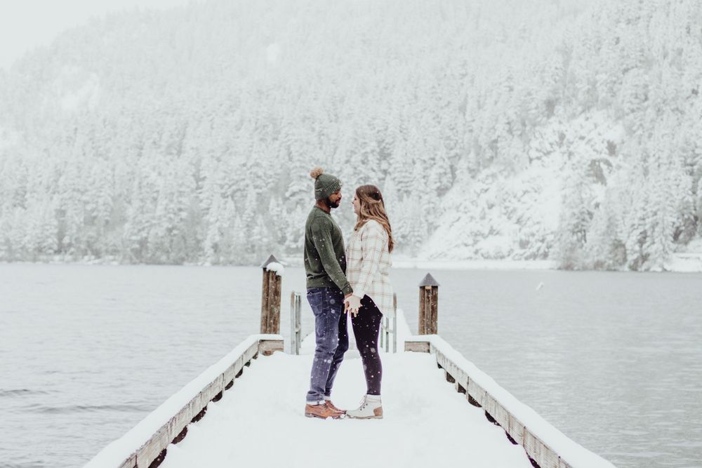 A couple holds hands and talks to each other in the snow on a pier during an engagement session with Pamela Clark