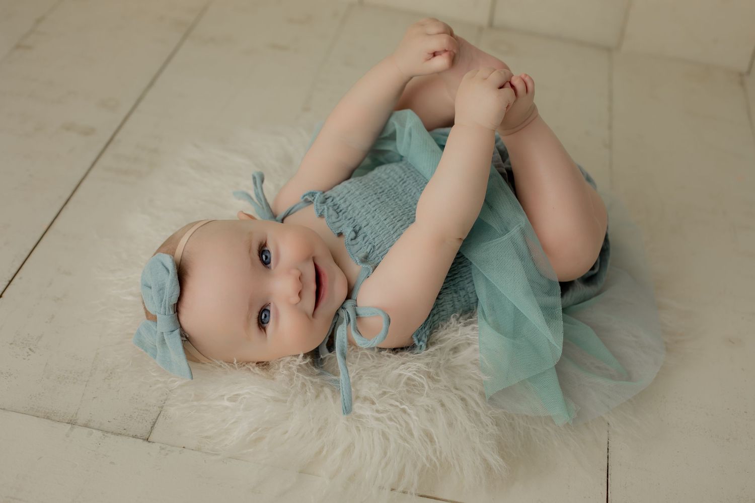 Baby girl grabs her toes and smiles for her six month milestone in the photography studio.