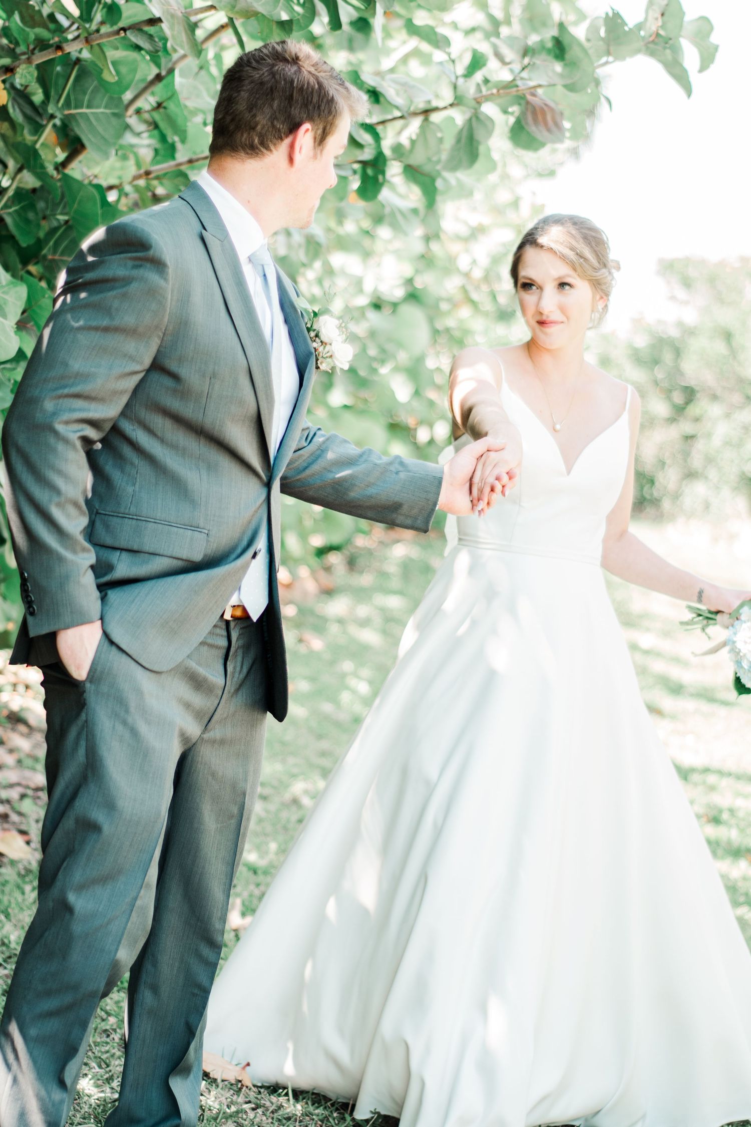 A couple poses outdoors for a romantic wedding photo with the bride in a flowing white gown and groom in gray suit.