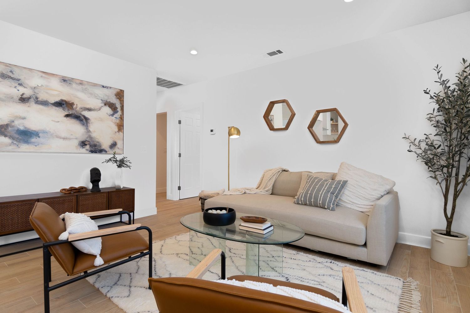 Contemporary living room with neutral sofa, hexagonal wall decor, and leather accent chairs.