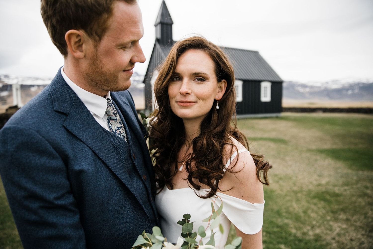 A romantic portrait of a wedding couple standing outdoors with a black church in the background.