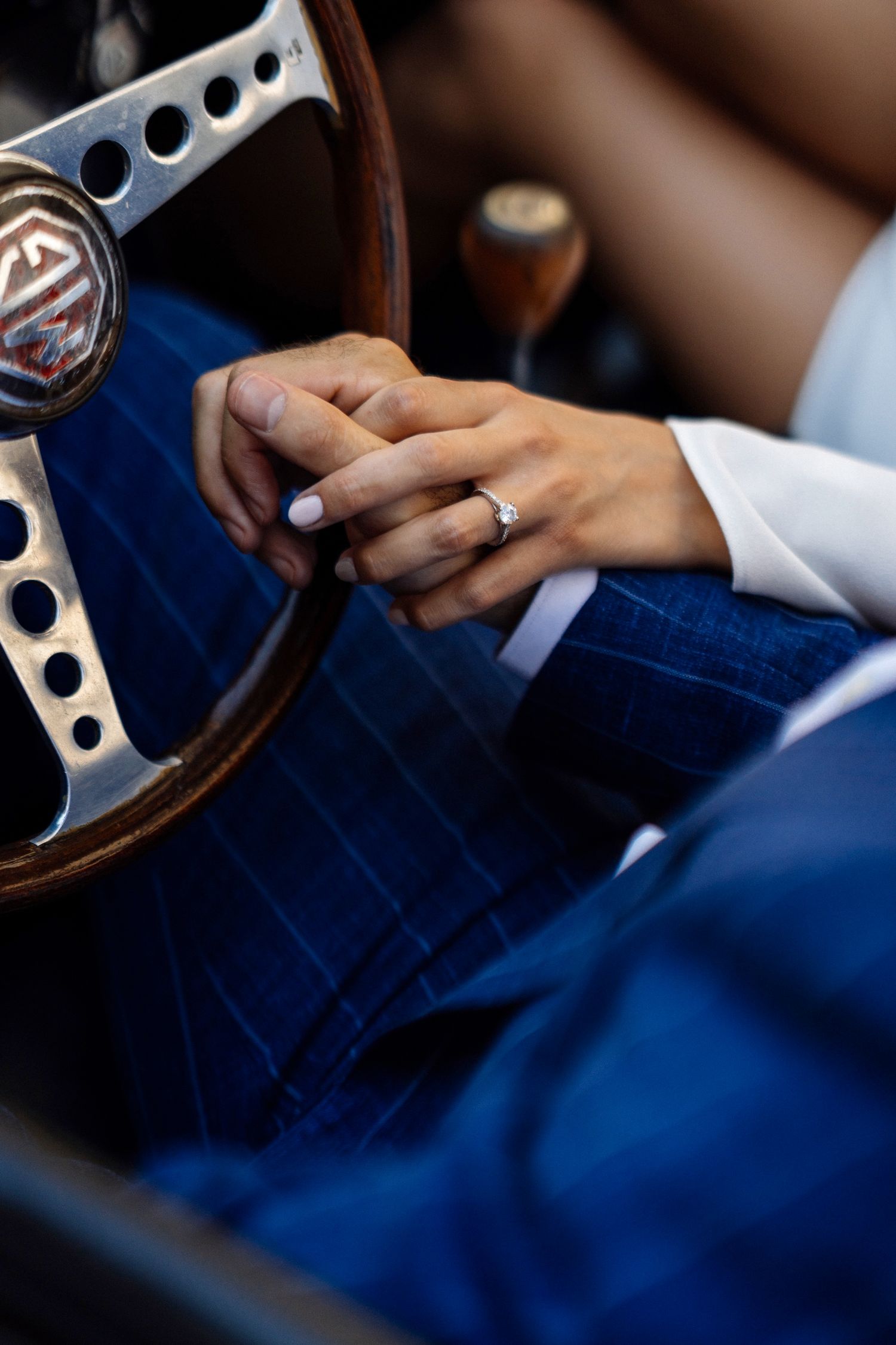 Close up of hands on a vintage steering wheel showing an engagement ring.