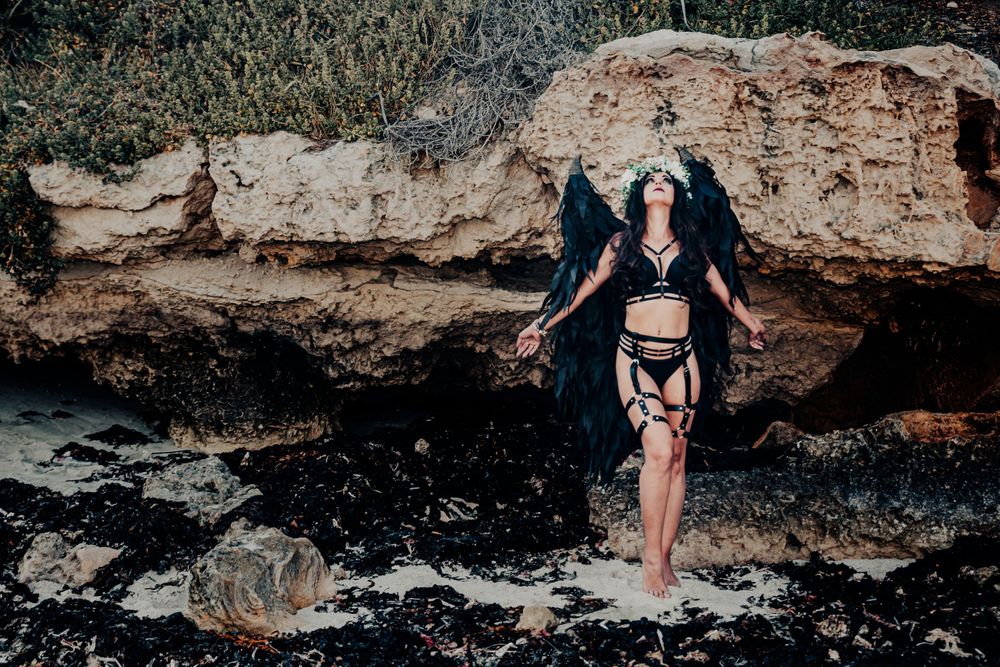 Artistic beach portrait with black feathered wings and rocky coastal background.