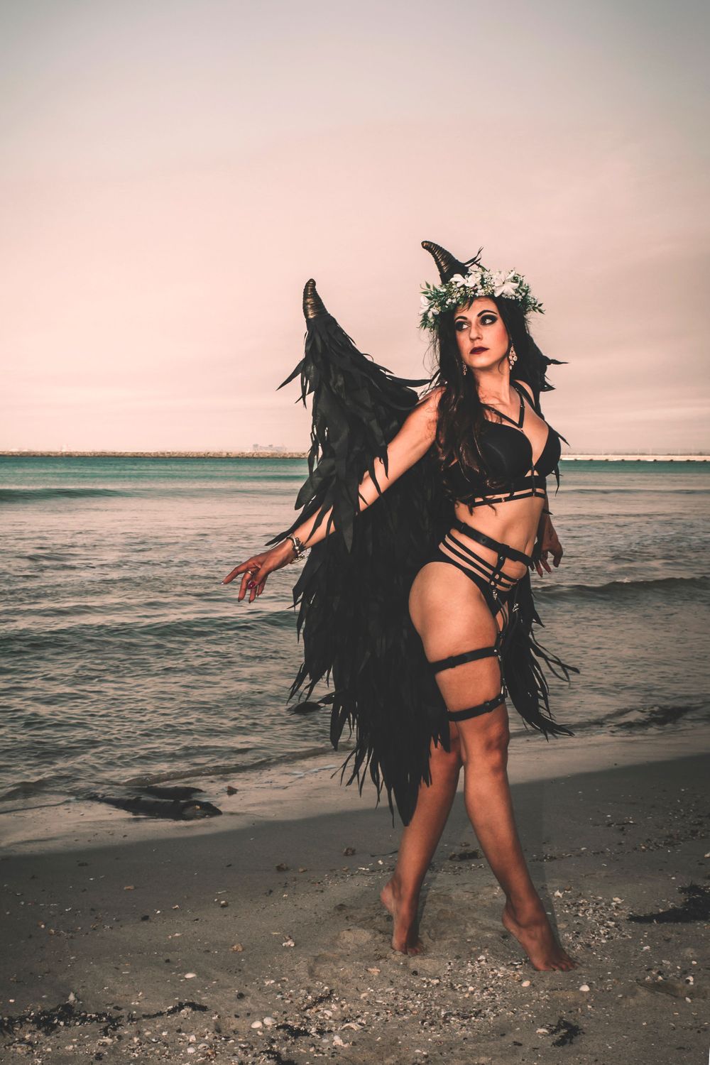 Dynamic beach photoshoot featuring black wings and expressive dance movements at sunset.