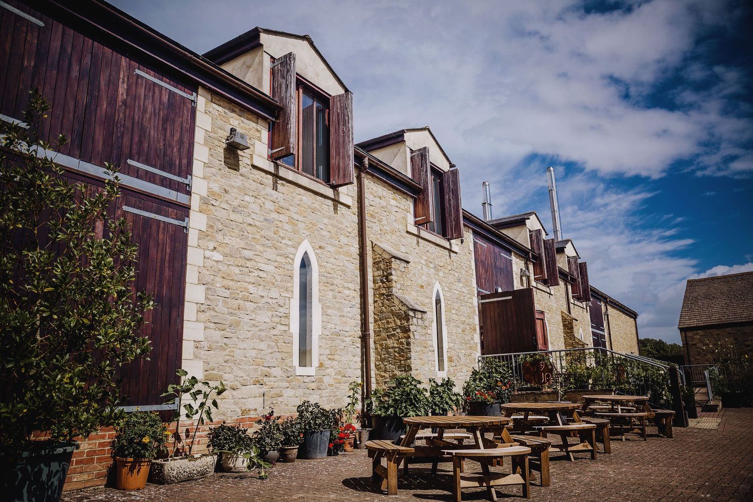 Historic stone building with burgundy accents and outdoor picnic tables along its facade.