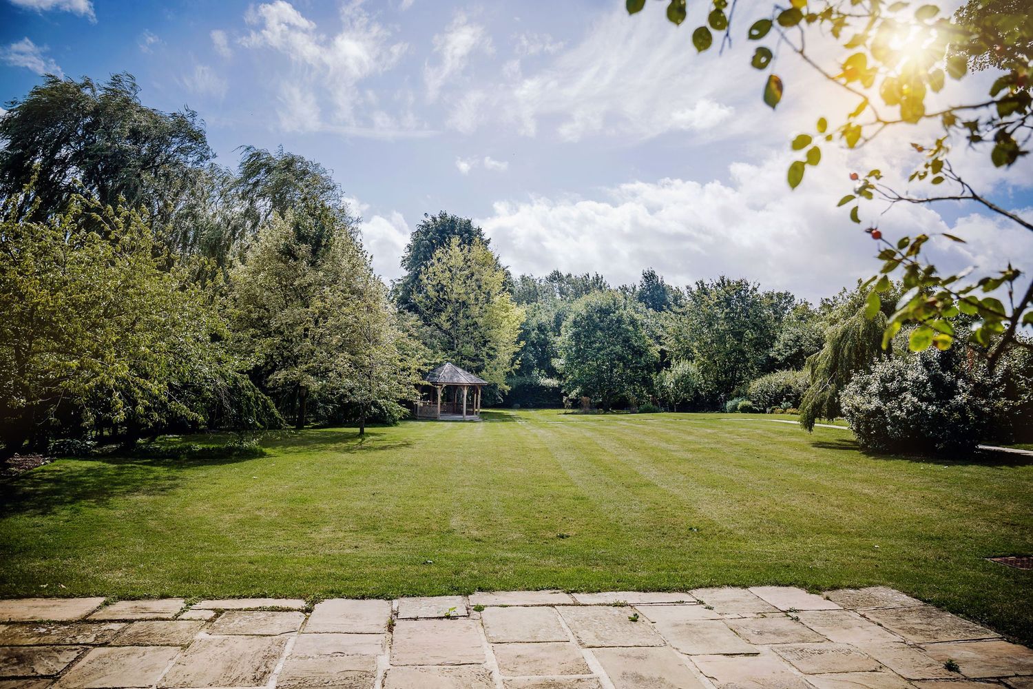 Manicured green lawn with stone patio and surrounding trees under cloudy skies.