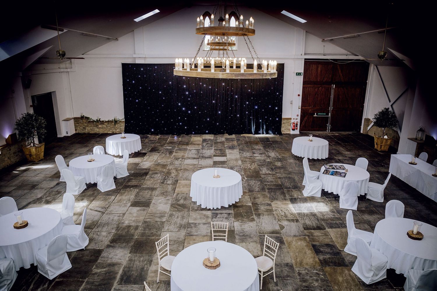 Event space decorated with white round tables and a chandelier against a starry backdrop.