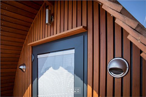 Modern wooden cabin exterior featuring vertical timber slats, a gray door and circular porthole window.