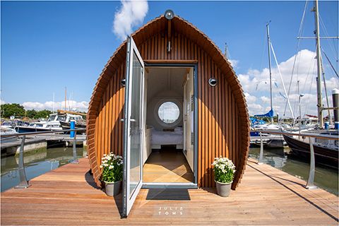 Unique barrel-shaped floating pod with wooden exterior and glass door entrance at a marina.