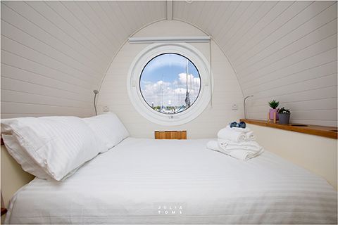 Cozy white bedroom interior with porthole window offering marina views and crisp bedding.