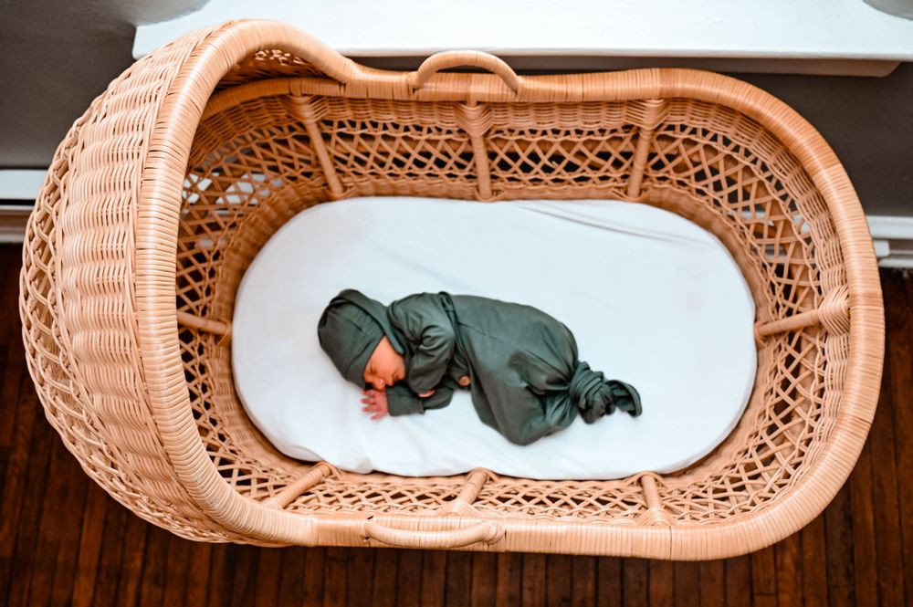 A woven bassinet with white bedding sits ready for a baby.