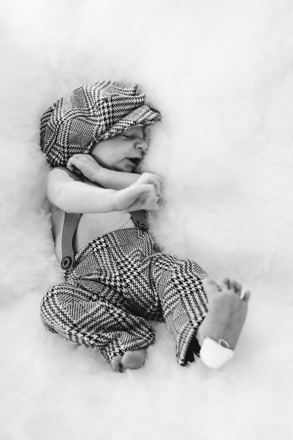 Baby sleeping in checkered outfit on white background.