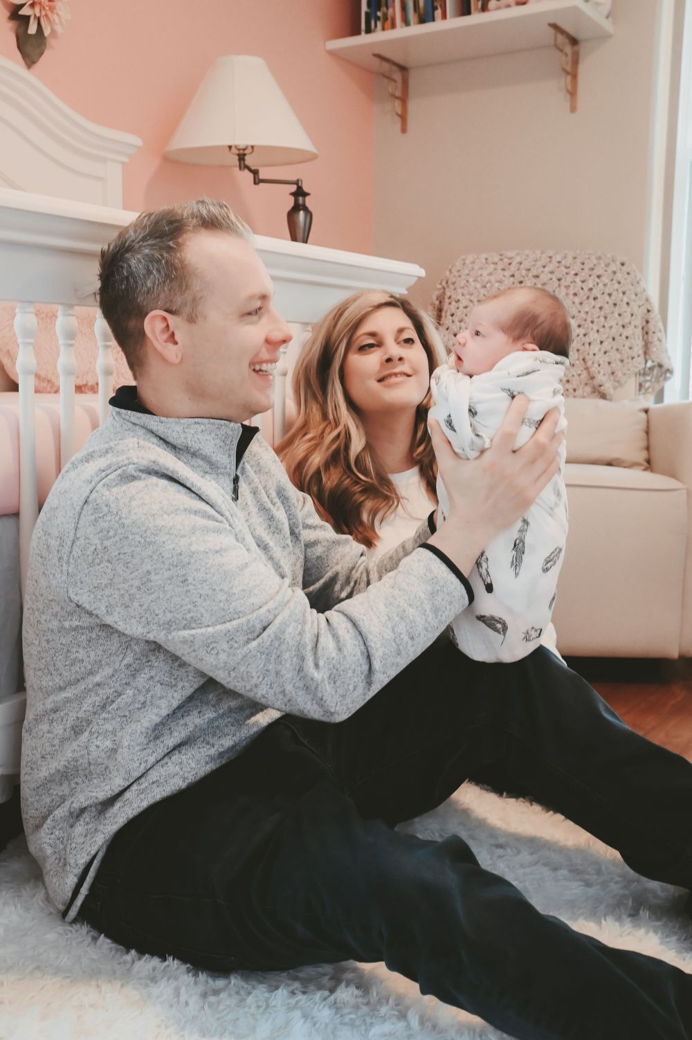 Parents lying on floor playing with their baby in a cozy nursery setting.