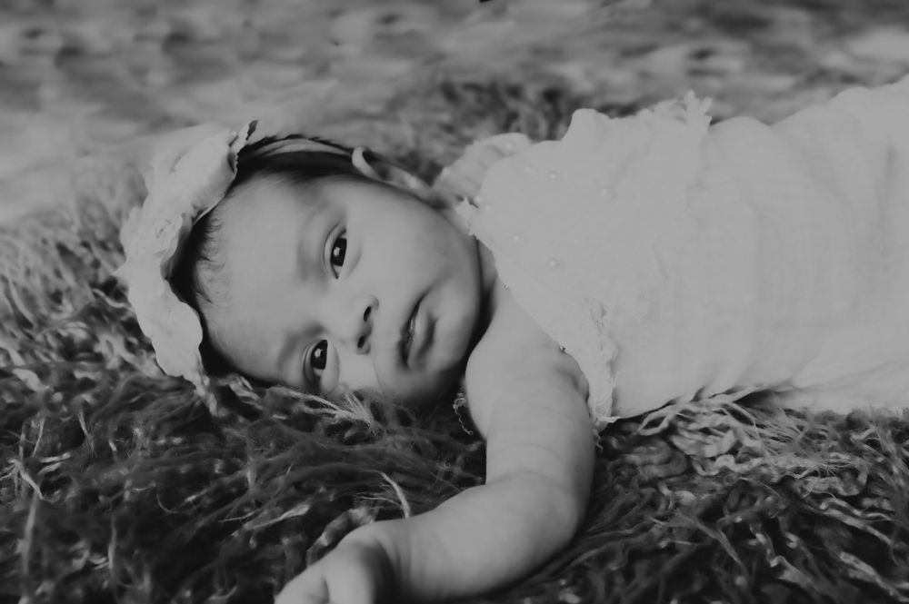 Black and white portrait of baby lying on textured surface looking at camera.