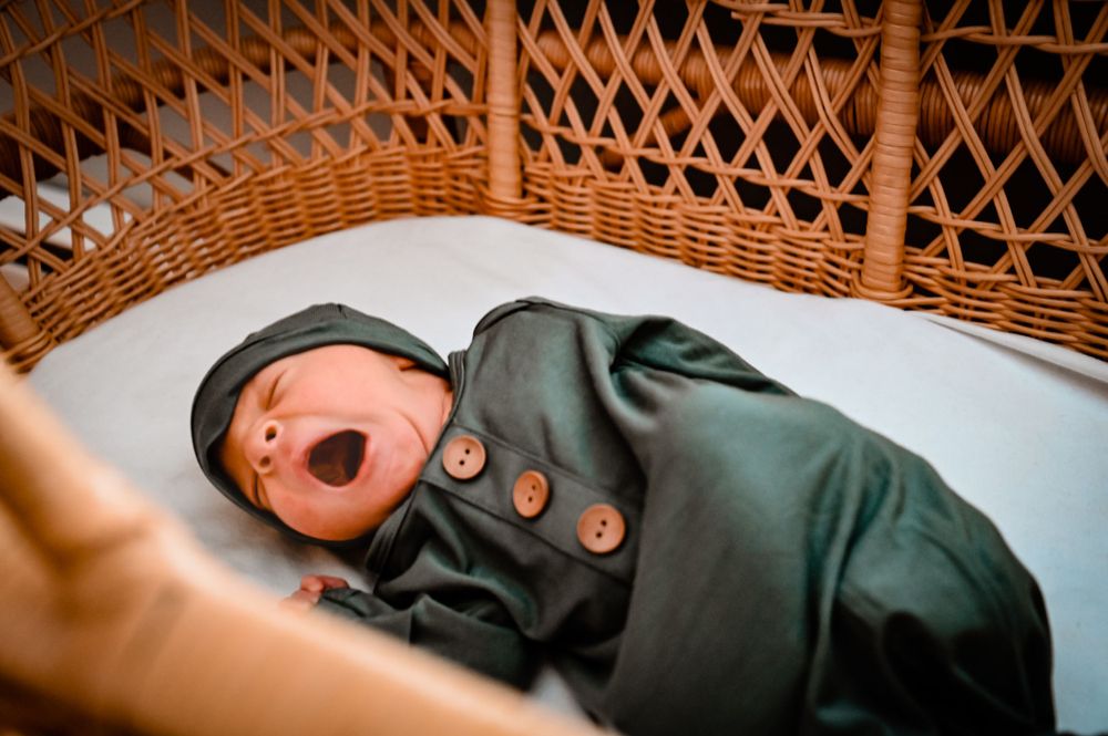 Sleeping baby in dark outfit lying in wicker bassinet.